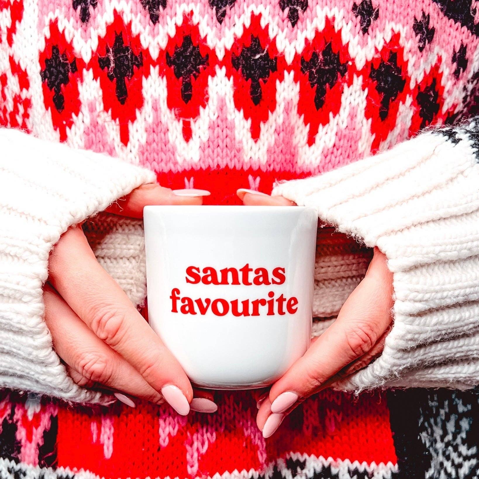 Weihnachtlicher Becher „Santas Favourite“ von Frau Hansen – weißer Porzellanbecher ohne Henkel mit roter Aufschrift, gehalten von einer Frau im roten Weihnachtspullover. Perfekte Geschenkidee und stilvolle Weihnachtstasse für Kaffee, Tee oder Kakao.